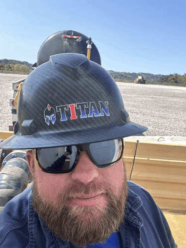 a man wearing sunglasses and a hard hat that says titan