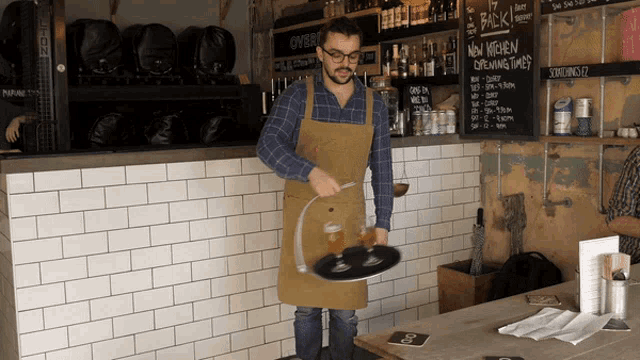 a man in an apron carrying a tray of beer in front of a chalkboard that says new kitchen brewing times