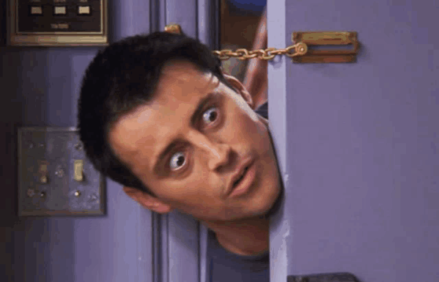 a man is peeking out from behind a door with a lock on it