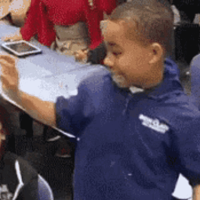 a young boy in a blue shirt is standing in front of a table with a tablet in the background .