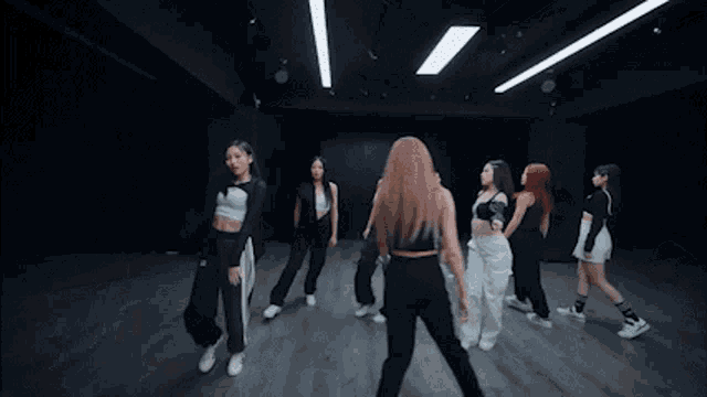 a group of women are dancing in a dark room and one of them is wearing a white adidas top