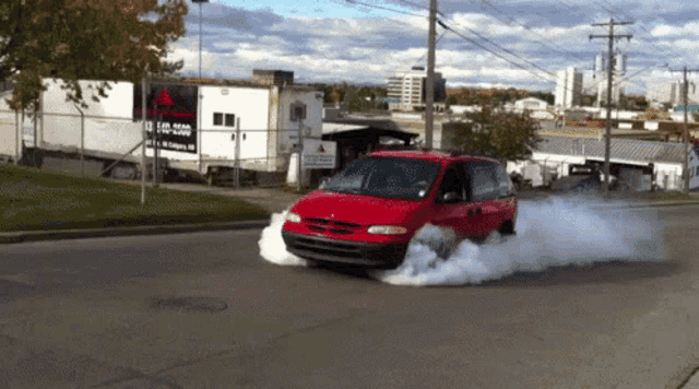 a red minivan is driving down a street with smoke coming out of it