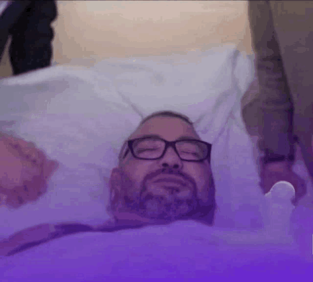 a man with glasses laying in a hospital bed