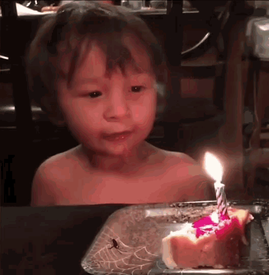 a little boy is sitting at a table with a piece of cake and a lit candle on it .