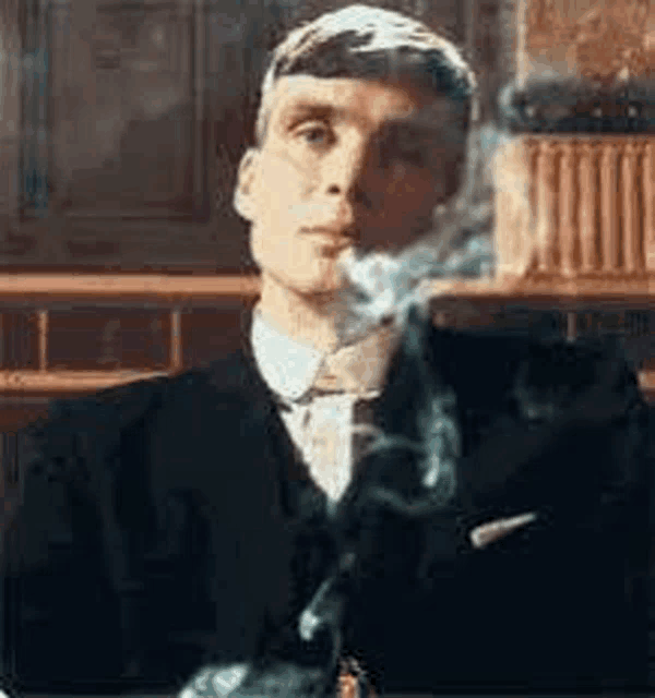 a man in a suit and tie is smoking a cigarette while sitting at a table .