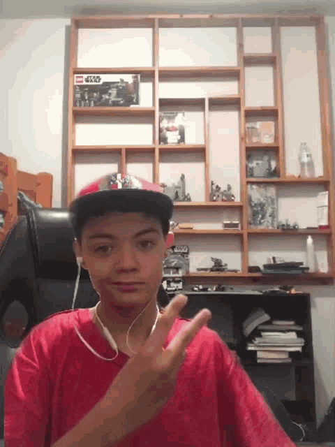 a boy wearing a red shirt and a hat with a lego star wars box on the shelf behind him