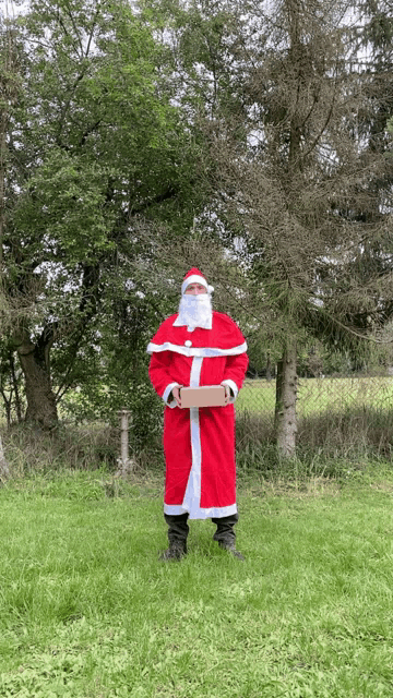 a man dressed as santa claus is holding a cardboard box in a field