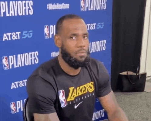 a man wearing a black lakers shirt is sitting in front of a blue wall