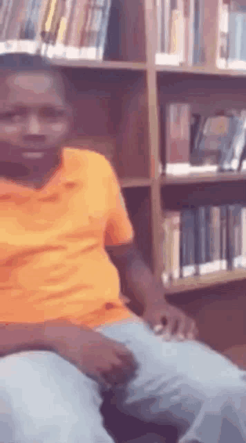 a man in an orange shirt is sitting in a library .