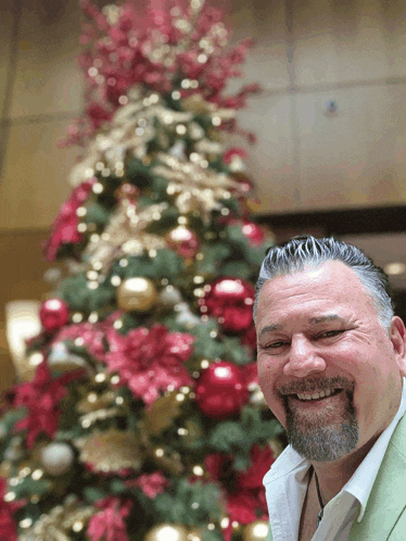 a man with a beard smiles in front of a decorated christmas tree