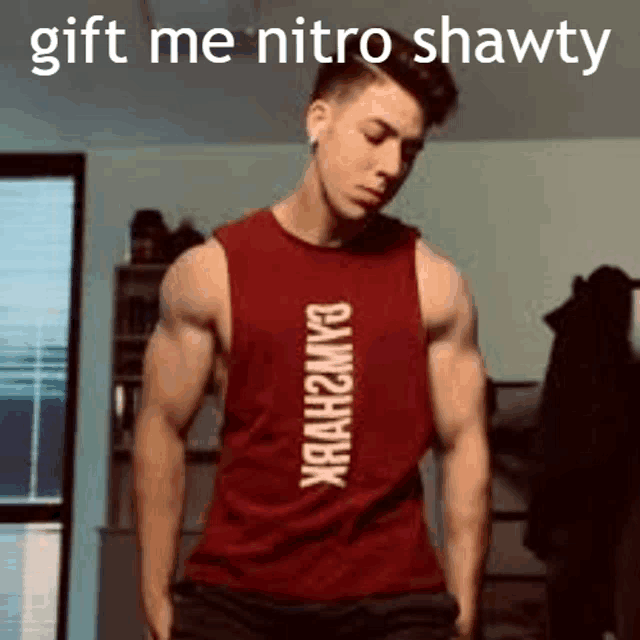 a man in a red tank top with the words `` gift me nitro shawty '' on it is standing in a room .