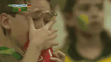 a man wearing glasses is drinking from a coca cola bottle while watching a soccer game between brazil and germany