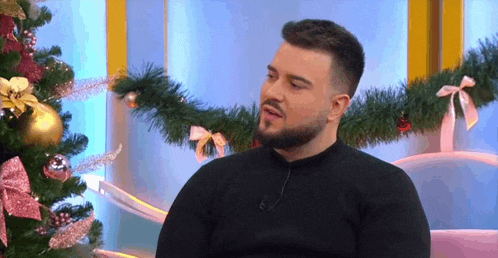 a man is sitting in front of a christmas tree