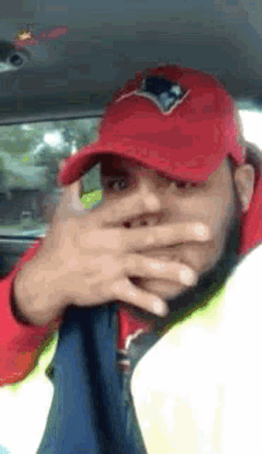 a man wearing a red patriots hat covering his face with his hand