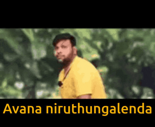 a man in a yellow shirt is standing in front of trees with the words avana niruthangalenda written on the bottom .