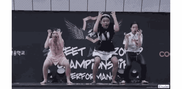 three girls are dancing in front of a sign that says champions