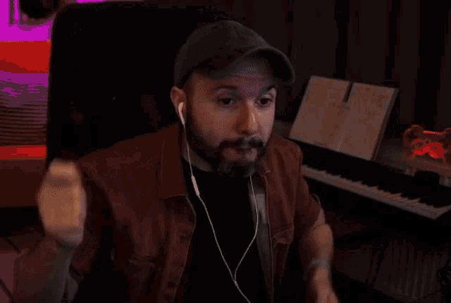 a man with a beard wearing ear buds and a hat is pointing at the camera