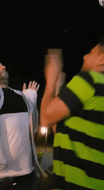 a man in a green and black striped shirt is standing next to another man in a white shirt