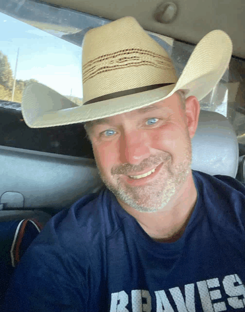 a man wearing a cowboy hat and a braves shirt is smiling