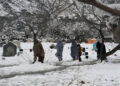 People walk past graves after heavy snowfall. — AFP/File