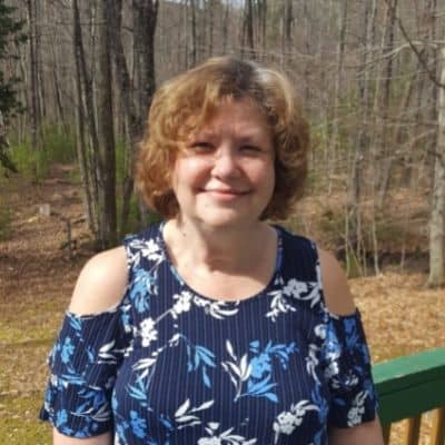 smiling brown haired woman in blue flowered shirt, one exceptional life owner