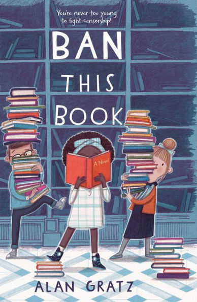 Book cover showing three people standing in front of a large bookshelf largely emptied of books.  Two white adults on the left and right a tall pile of books in their arms (with the man on the left having another tall pile on his head), while a Black girl in the center foreground has an open book obscuring most of her face, and one of her feet on a smaller pile of books.  Text above her head says 'BAN THIS BOOK'; text on the cover of the book she is reading sais 'A Novel'; text below her says 'Alan Gratz'.