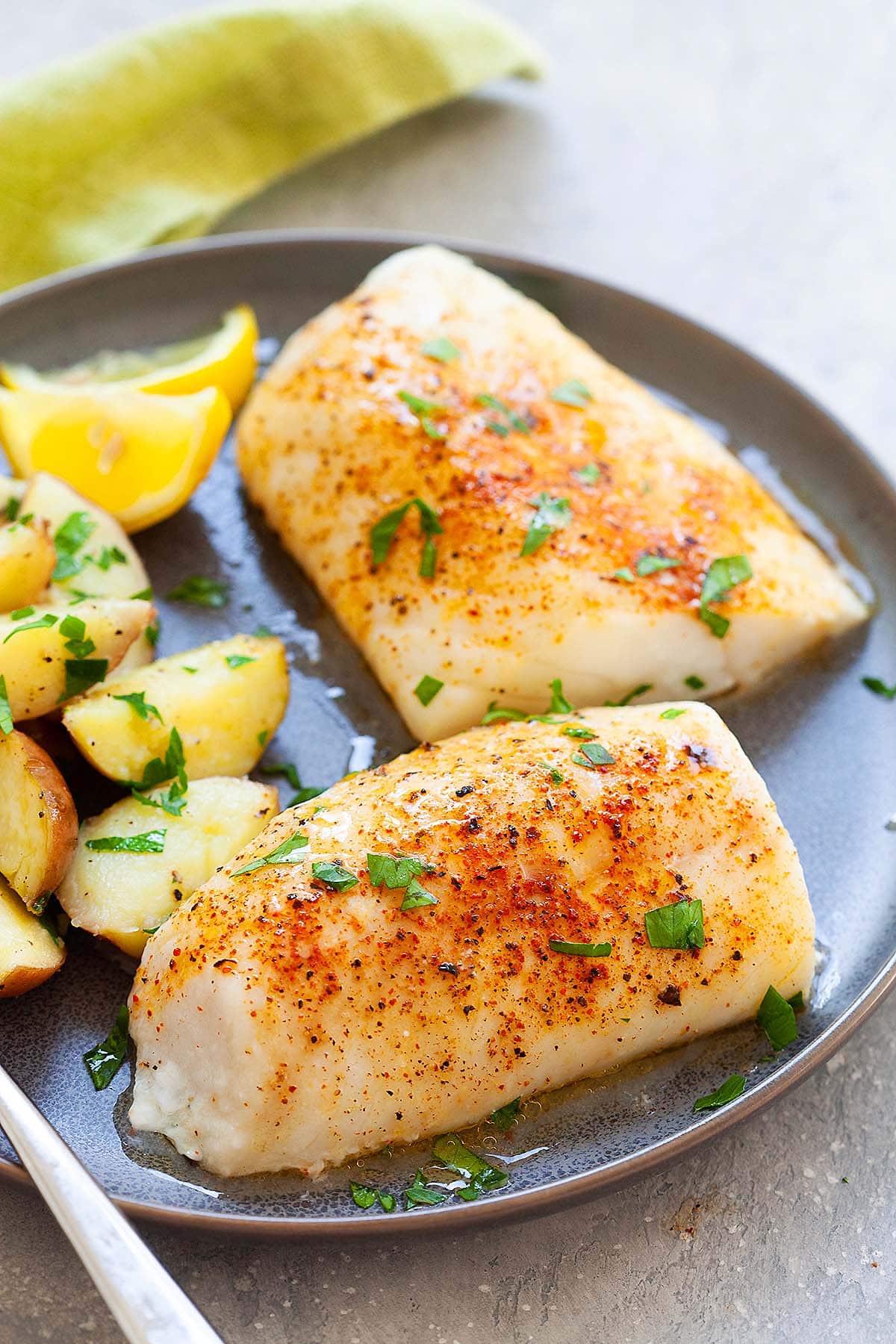 Freshly baked cod fillet with seasonings crust on a plate, garnished with lemon slices and herbs.