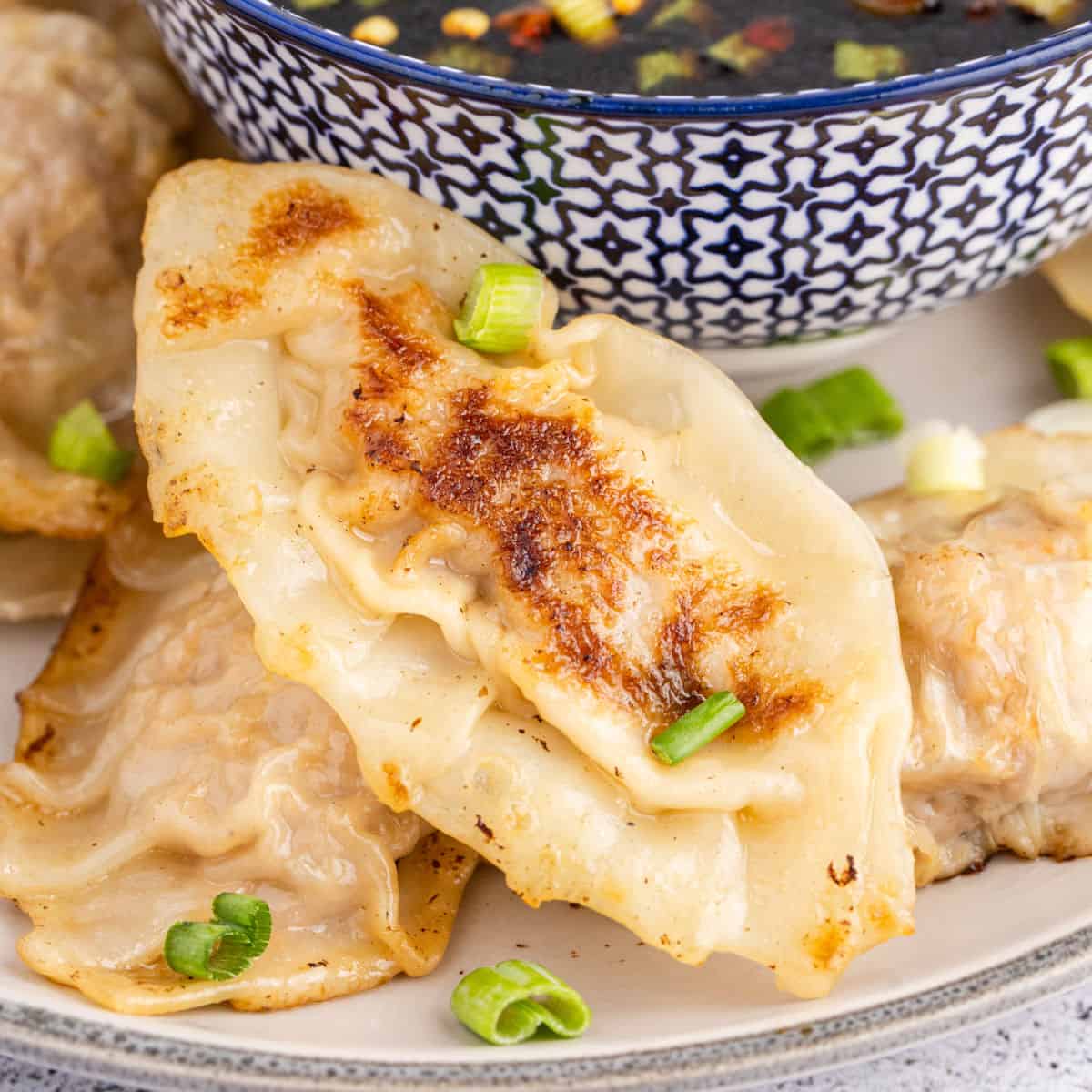 square image of potstickers on a plate next to a bowl of sauce