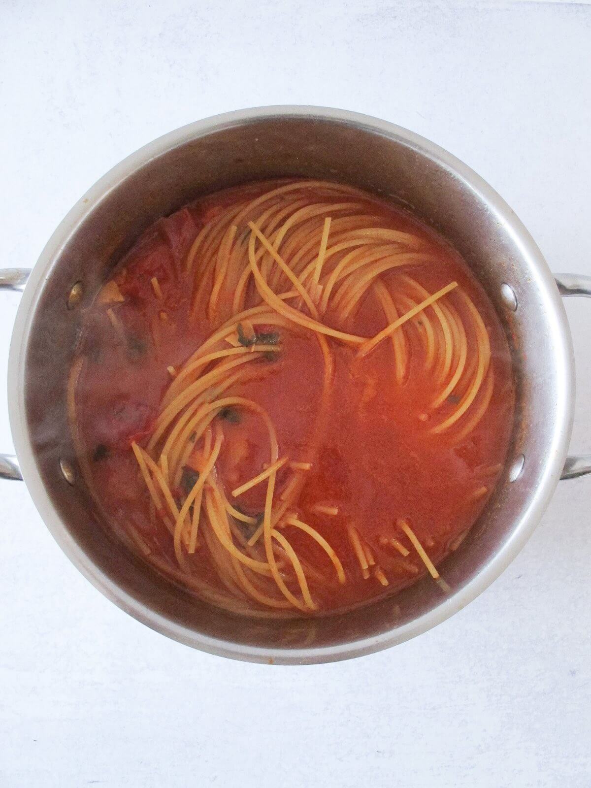 spaghetti cooking in a pot of spicy tomato sauce.