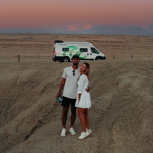 Couple standing together in a desert setting in front of a roadsurfer camper van at sunset