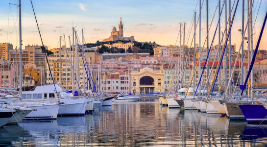 Yachts reflecting in the still water of the old Vieux Port of Marseilles beneath Cathedral of Notre Dame, France, on sunrise