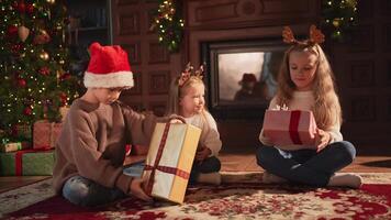 Merry Christmas Xmas holiday. Children unpacking open up gift box near Christmas tree. Kids in living room with Christmas tree fireplace opening gift box with surprise faces. Christmas eve at home video