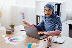 Modern Profession. Portrait of busy arabic female graphic designer working on new project with color swatches and laptop in office, free space photo