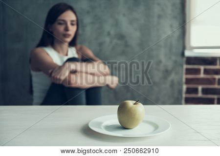 Woman Sitting On Chair And Eating One Apple. Diet Concept. Weight Loss Problem. Starving Young Woman