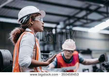 Female Industrial Engineer Wearing A White Helmet While Standing In A Heavy Industrial Factory Behin