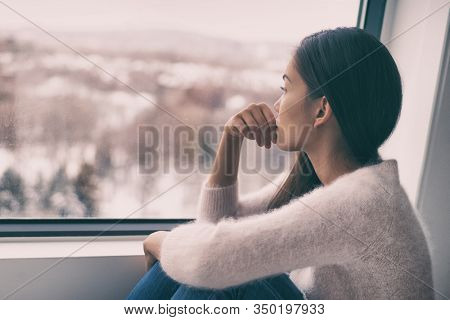 Winter depression - seasonal affective disorder mental health woman sad comtemplative looking out the window alone.