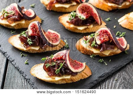 Canape or crostini with toasted baguette cheese onion jam figs and fresh thyme on a slate board. Delicious appetizer ideal as an aperitif. Selective focus