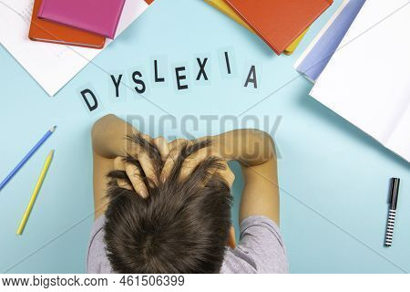 Sad Tired Frustrated Teenage Boy Sitting At Table With Many Books And School Supplies. Word Dyslexia