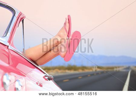 Freedom car travel concept - woman relaxing with feet out of window in cool convertible vintage car. Girl relaxing enjoying free holidays road trip.