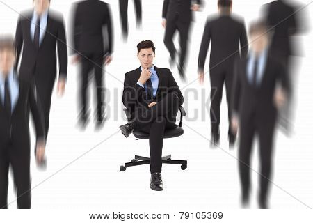 Young Businessman Sitting In A Chair And People Walking Through