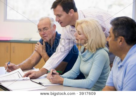 Adult Students In Class With Teacher Helping (Selective Focus)