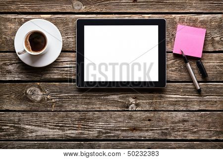 Digital tablet computer with sticky note paper and cup of coffee on old wooden desk. Simple workspace or coffee break with web surfing.