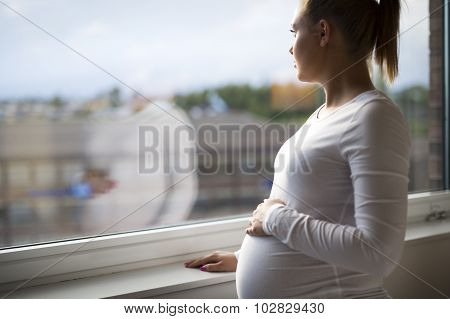 Thoughtful pregnant woman looking out the window