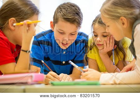 education, elementary school, learning and people concept - group of school kids with pens and papers writing in classroom