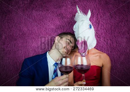 Portrait Of Unusual Couple On Purple Background. Freaky Young Woman In Comical Mask Drinking Wine Wi