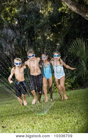 Children Running Through Lawn Sprinkler Together