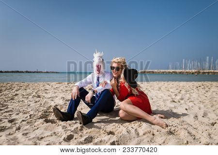 Young Happy Woman Sits With Businessman In Funny Mask. Strange Guy In Suit Sits With Beautiful Girl 