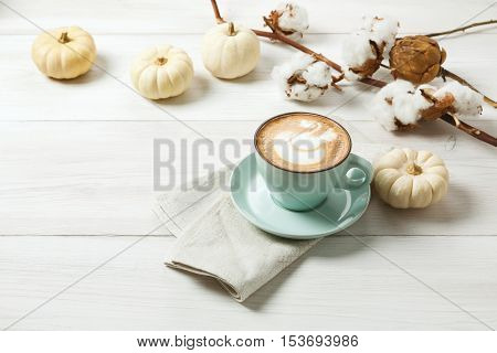 Pumpkin spice latte. Blue coffee cup with creamy foam, cinnamon sticks, autumn sloe and small yellow pumpkins at white wood background. Fall hot drinks, cafe and bar concept