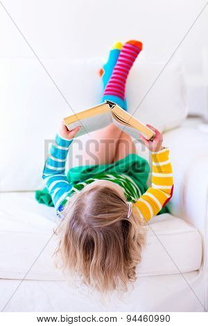 Little Girl Reading A Book On A White Couch