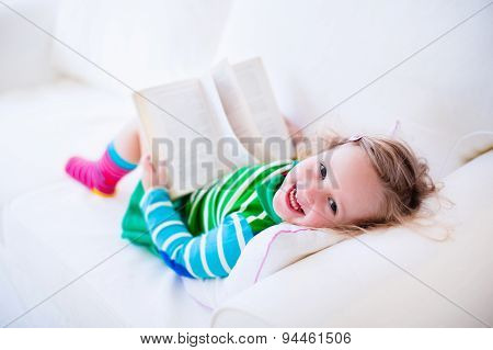 Little Girl Reading A Book On A White Couch